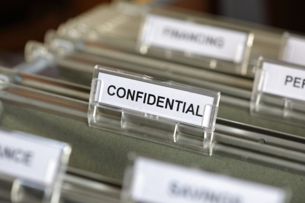 Inside of a filing cabinet with green folders and focus on confidential label