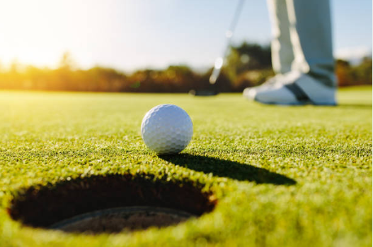 Golf ball rolling to a cup with shoes and putter in the background