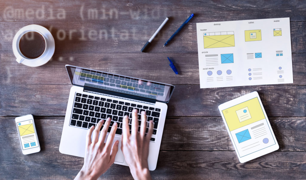 Webdesigner sketching responsive website wireframe with laptop, smartphone and tablet