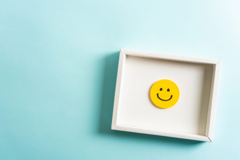 Concept of well-being, well done, feedback, employee recognition award. Happy yellow smiling emoticon face frame hanging on blue background with empty space for text.